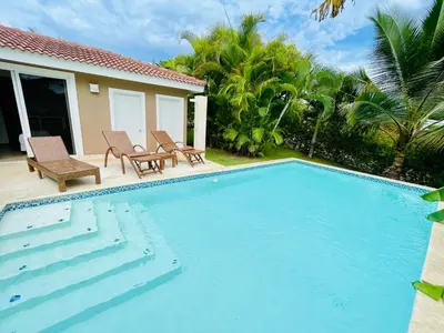 a swimming pool with two chairs and a house at Casa feliz in Sosúa
