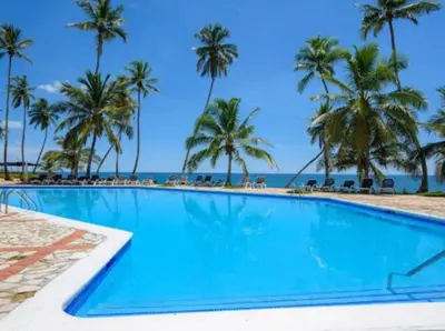a swimming pool with palm trees and the ocean at Estancia Nana apartamento vista al mar piscina WIFI cocina completa aire acondicionado Lavadora secadora in Juan Dolio