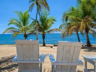 two chairs and a table on a beach with palm trees at Estancia Nana apartamento vista al mar piscina WIFI cocina completa aire acondicionado Lavadora secadora in Juan Dolio