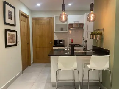a kitchen with a counter and two white chairs at Apartmento en el corazón de la ciudad con piscina infinita y vista al mar in Santo Domingo