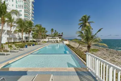 a swimming pool next to a beach with palm trees at El Retiro Juan Dolio Beach by Elital Luxury in Villas del Mar