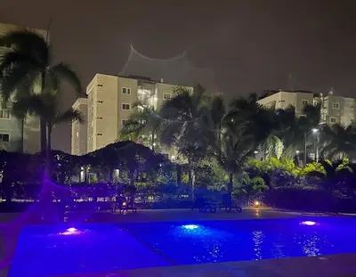 a swimming pool at night with palm trees and buildings at Residencial Mediterraneo in Santiago de los Caballeros