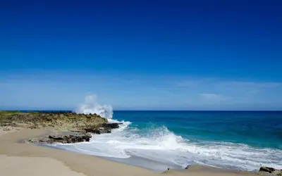 a beach with a wave hitting the shore with the ocean at Blue fish apartamento in Sosúa