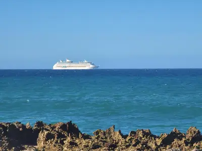 a cruise ship in the ocean with rocks in the foreground at Blue fish apartamento in Sosúa
