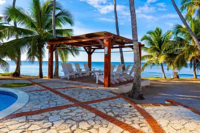 a gazebo on the beach with palm trees and the ocean at OCEANPARADISE to you ALBATRO l Y ll in Juan Dolio