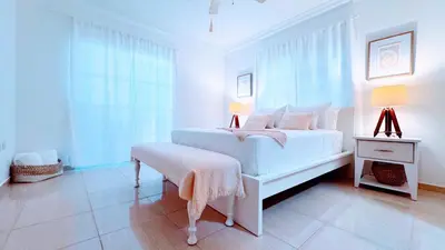 a white bedroom with a white bed and a window at Walk to Beach, Shops, Dining, Pool View, Fast Wifi in Punta Cana
