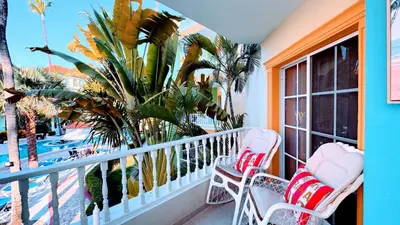 a balcony with two chairs and a palm tree at Walk to Beach, Shops, Dining, Pool View, Fast Wifi in Punta Cana