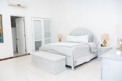 a white bedroom with a white bed and a table at Cacique 13, Ocean View and Golf Course in La Romana