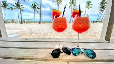 two glasses of juice and a pair of sunglasses on a beach at Backyard, Pool View, Walk to Beach, Dining, Shops in Punta Cana