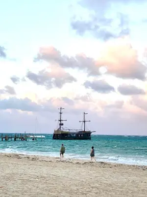 two people walking on the beach with a boat in the water at Central in Punta Cana Beach Life RD in Punta Cana