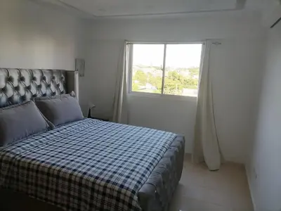 a bedroom with a bed with a checkered blanket and a window at Quiet apartment, good access to Supermarkets, Center etc in Santo Domingo