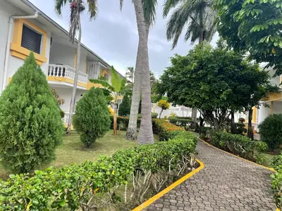 a walkway in front of a building with trees and bushes at Kasita del sol boca chica in La Caleta