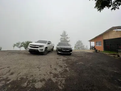 two trucks parked in a dirt lot next to a building at Vista Montaña Jimenoa de la Rosa in Jarabacoa
