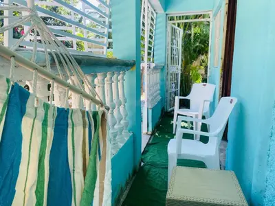 a balcony with a hammock and chairs on a blue house at Rincón del Mojito in Santa Cruz de Barahona
