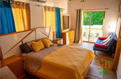 a bedroom with a bed and a chair and a window at Villa del Bosque, Vacacional Matua in La Piña