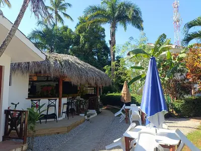 a resort with a thatched building with chairs and a umbrella at Cozy studio- centre - near beach in Las Terrenas