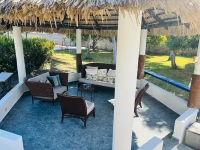 a patio with a couch and chairs under a straw umbrella at Villa Rosa Bella Perfect for families or groups in Palmar de Ocoa