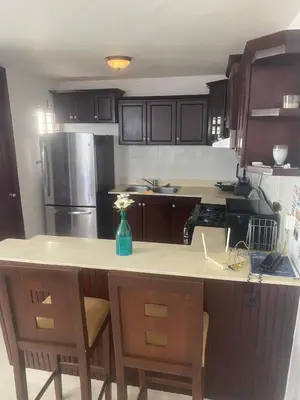 a kitchen with wooden cabinets and a counter with a vase of flowers at Cozy, comfortable three-bedroom condo in Santiago,DR in Santiago de los Caballeros