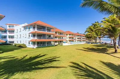 a large building with palm trees in front of the ocean at Oceanfront Apartment in Cabarete with Pool and Beach Access in Cabarete