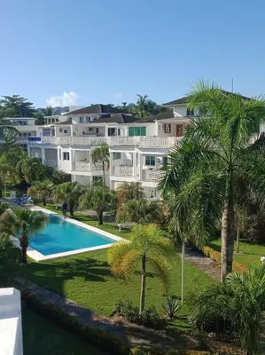 a large white house with a swimming pool and palm trees at Apartment mit Meerblick direkt an der Playa Popy in Las Terrenas