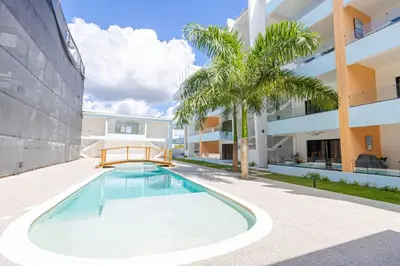 a swimming pool in front of a building with a palm tree at Serene 2-Bedroom Coastal Retreat in Bayahibe in San Rafael del Yuma