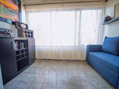 a living room with a blue couch and a large window at Colonial 2BR Apartment 2mins walk to beach in Sosúa