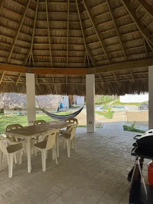 a table and chairs under a straw roof with a hammock at Charming Bungalow with Pool in Sosúa