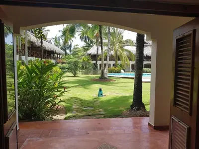 an open door to a yard with a pool and palm trees at Lovely Beach Apartment in Tranquil Playa Bonita in Las Terrenas