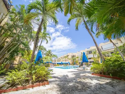a resort pool with palm trees and blue umbrellas at Garden Condos 7 - Central Apartment in Strip in Sosúa