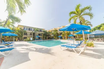 a swimming pool with chairs and blue umbrellas at Garden Condos 7 - Central Apartment in Strip in Sosúa