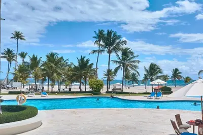 a resort pool with palm trees and the beach at Escape Beachfront Condo Costa del Sol Juan Dolio in Los Corrales