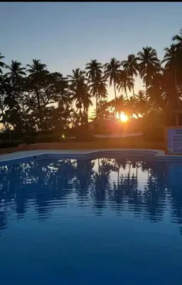 a swimming pool with palm trees and the sunset at villas bahia in Sánchez