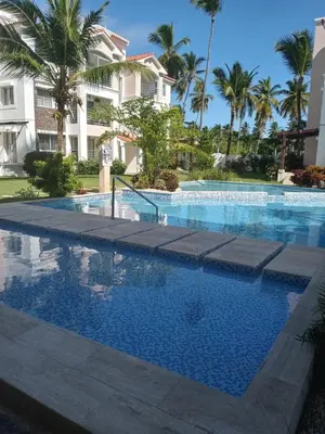 a swimming pool in front of a building with palm trees at Jojo's Caribbean Retreat in Punta Cana