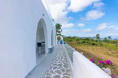 a white building with a porch with purple flowers at Grecialandia in San Felipe de Puerto Plata