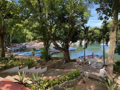 a woman sitting on a bench next to a river with boats at Room 4 in Río San Juan