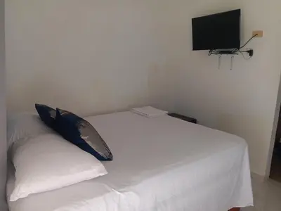 a white bed with a pillow and a flat screen tv at Hospedaje Las Flores Pedernales in Pedernales