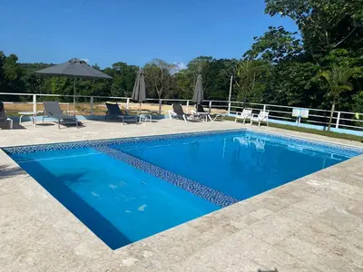 a blue swimming pool with chairs and umbrellas at Cozy Tropical Getaway in Los Altos de Jalisco