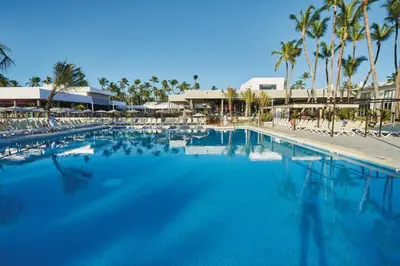 a large swimming pool with chairs and palm trees at Riu Bambu - All Inclusive in Punta Cana