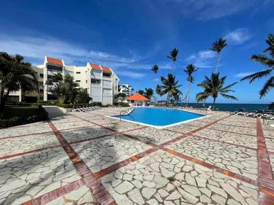 a resort swimming pool with palm trees and the ocean at Vista palmera in Juan Pedro
