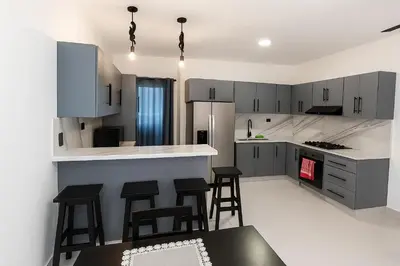 a kitchen with gray cabinets and black bar stools at Modern Serviced Apartment with Free Wi-Fi, 24h Power & Private Parking in Sosúa