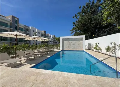 a swimming pool with chairs and umbrellas next to a building at Luxury first floor Apartment Pool kingside suite in Santiago de los Caballeros