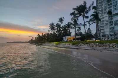 a beach with palm trees and a building and the ocean at Aquarella Caribbean Blue Summer Special GateAway in La Puntica de Juan Dolio