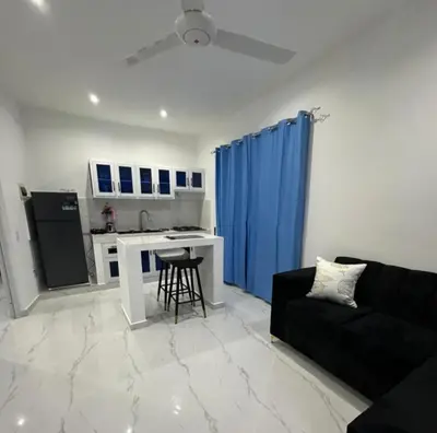 a living room with a black couch and a kitchen at Casi de Aleyda in Las Terrenas