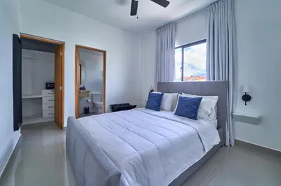 a white bedroom with a large bed with blue pillows at Cozy Nest in La Romana