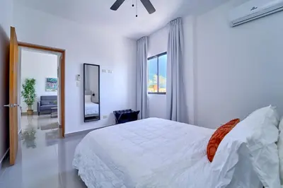 a white bedroom with a bed and a mirror at Cozy Nest in La Romana