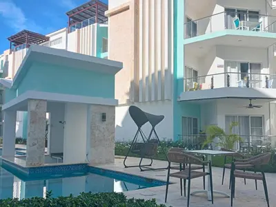 a building with a table and chairs next to a pool at Maple Beach Residences Punta Cana in Punta Cana