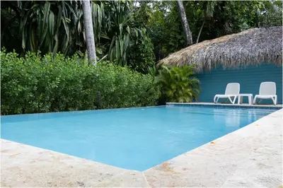 a swimming pool with two chairs and a hut at Escape Oasis in Playa Dorada Pool & Beach in Puerto Plata