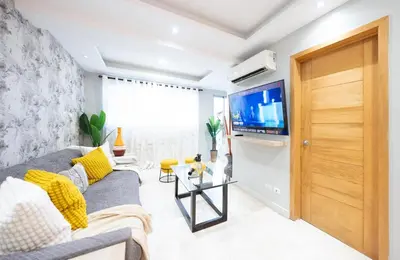 a living room with a gray couch and a tv at City Center, 2-BR Suite close to Shops, Restaurants, Bars and More in Santo Domingo