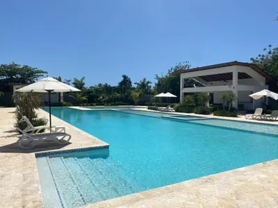 a large swimming pool with chairs and an umbrella at Coralclifftower in Juan Dolio