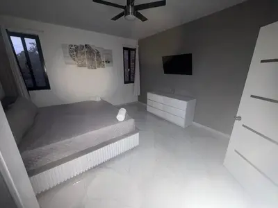 a white bedroom with a bed and a television at LEVEL suites in Sosúa